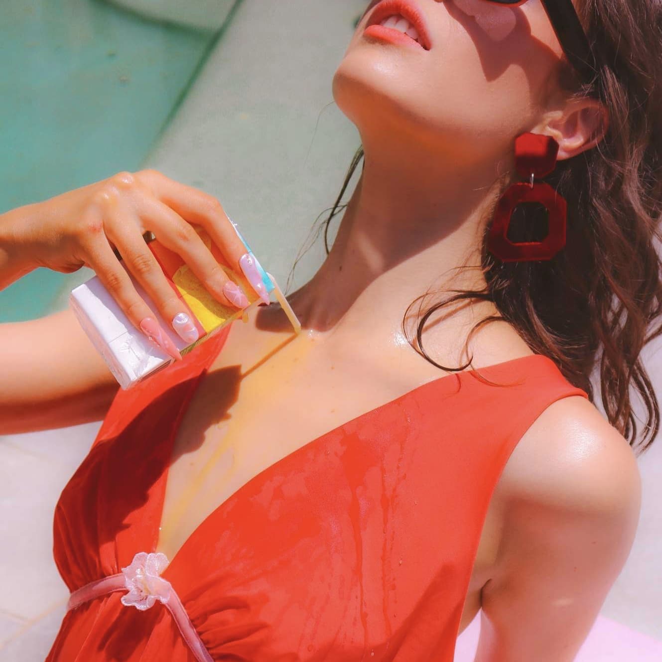 A faceless woman in a 70's style red dress pours orange juice over herself.