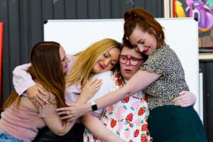 A group hug by the four female members of The Heartbreak Club, staged at The Paint Factory, during the 2026 Anywhere Festival (image credit: Creative Futures Photography).